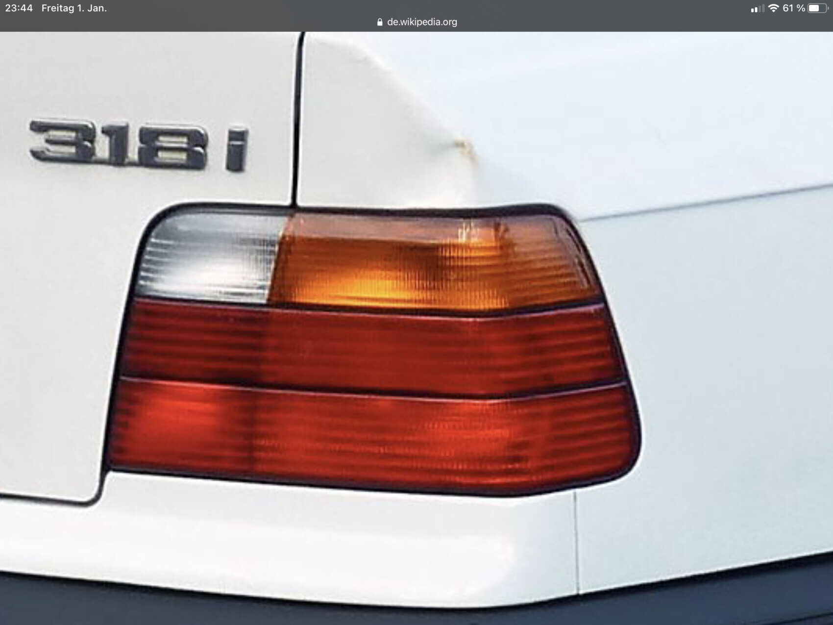 Rückleuchte eines weißen BMW 318i mit rotem und orangem Licht.