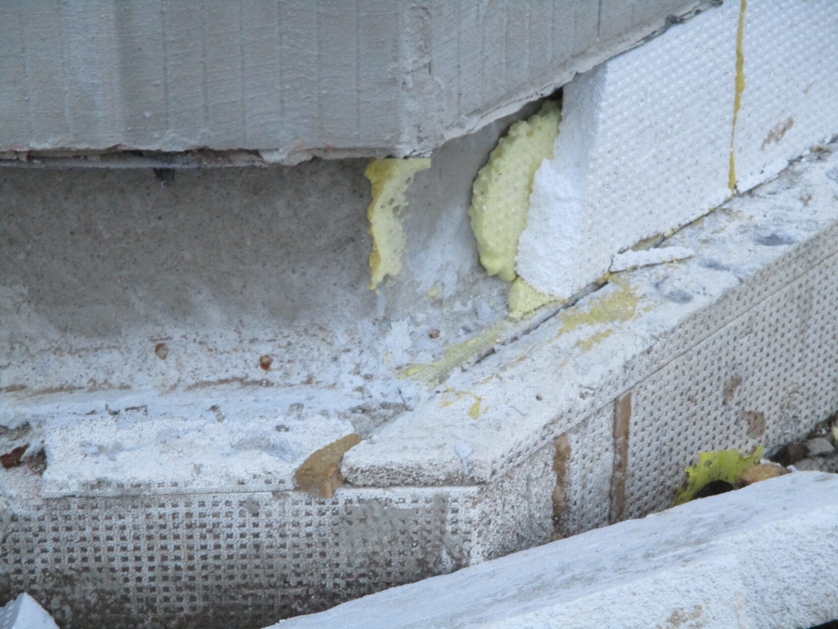Außenwand-Teil mit gelber Styropor-Dämmung, bröckelndem Putz und Betonfundament.