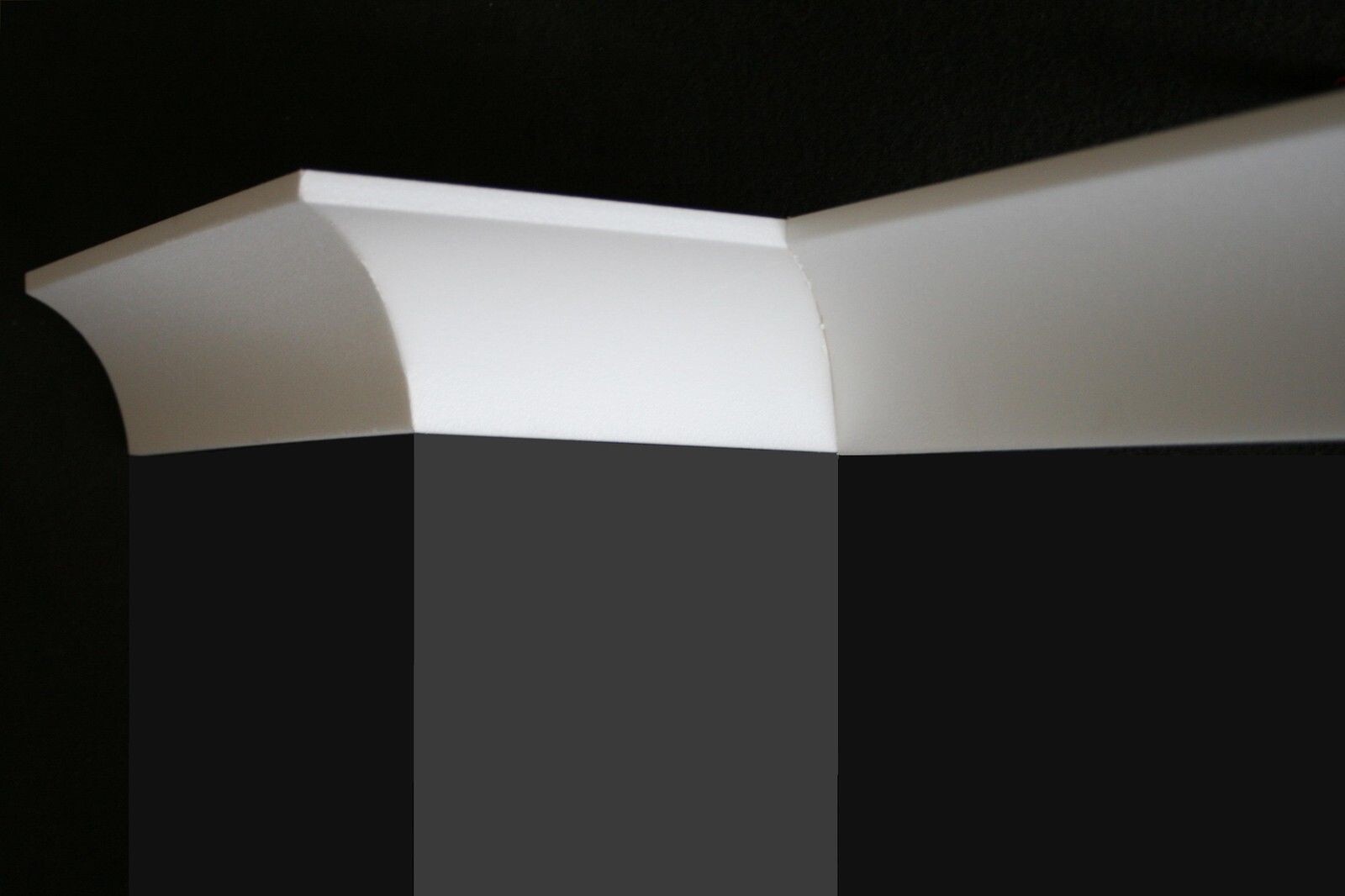 Weisse Deckenleiste aus Kunststoff mit Rundungen auf dunklem Hintergrund.