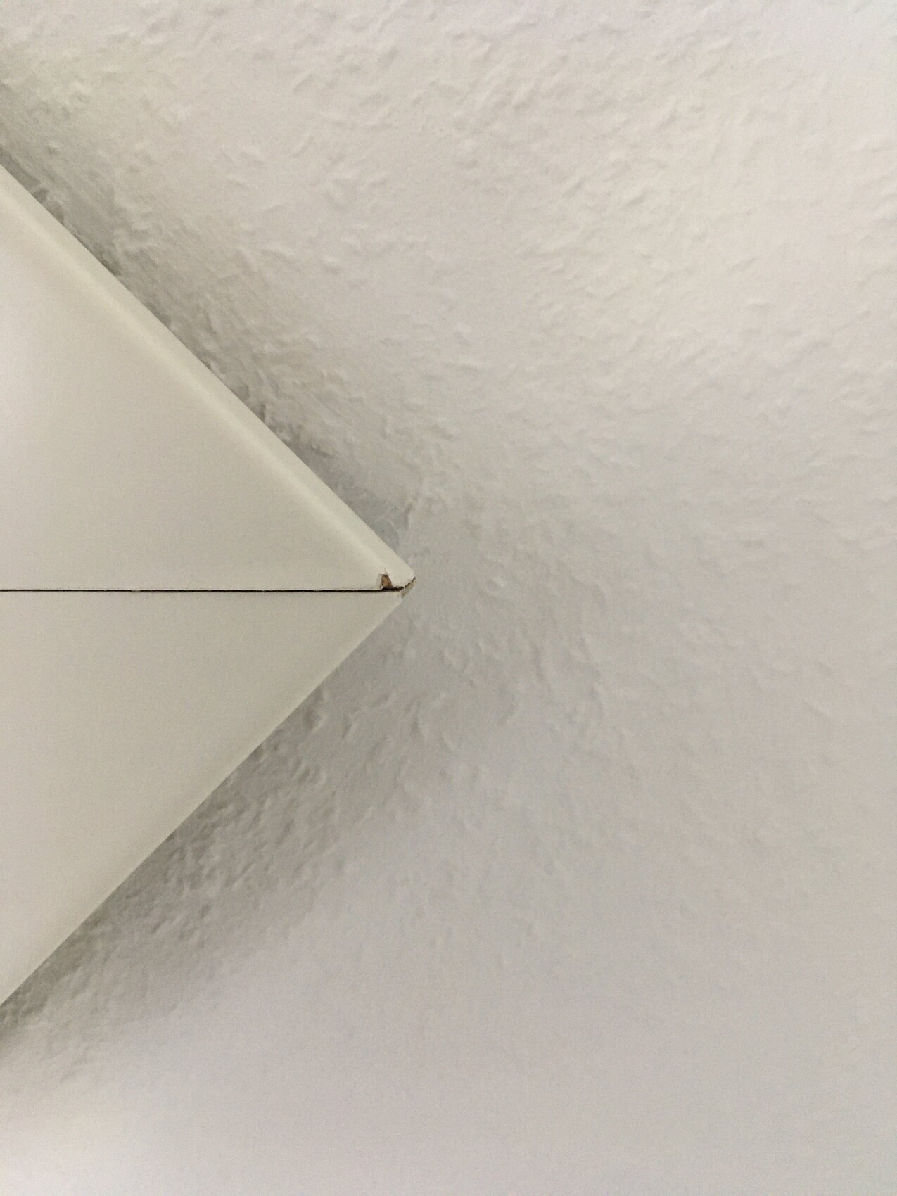 Schräge weiße Möbelkante vor texturierter Decke/Wand; kleiner brauner Fleck am Rand