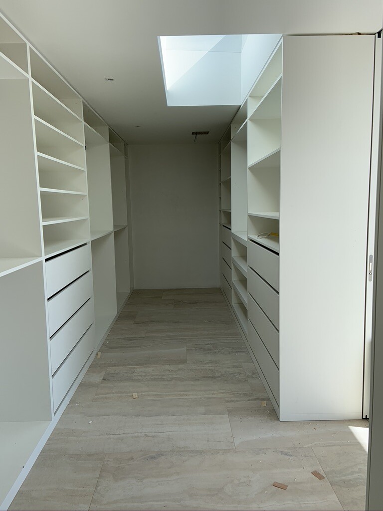 Begehbarer Kleiderschrank mit weißen Regalen und Schubladen beidseitig, Licht durch Oberlicht.
