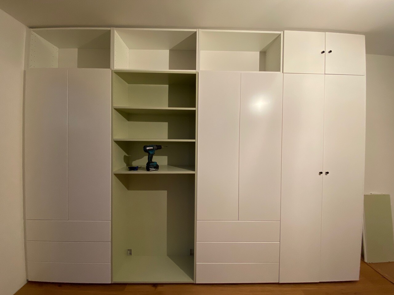 Weißes, großes Kleiderschrank-System mit offenen Fächern; Bohrmaschine liegt auf einer Regalebene.