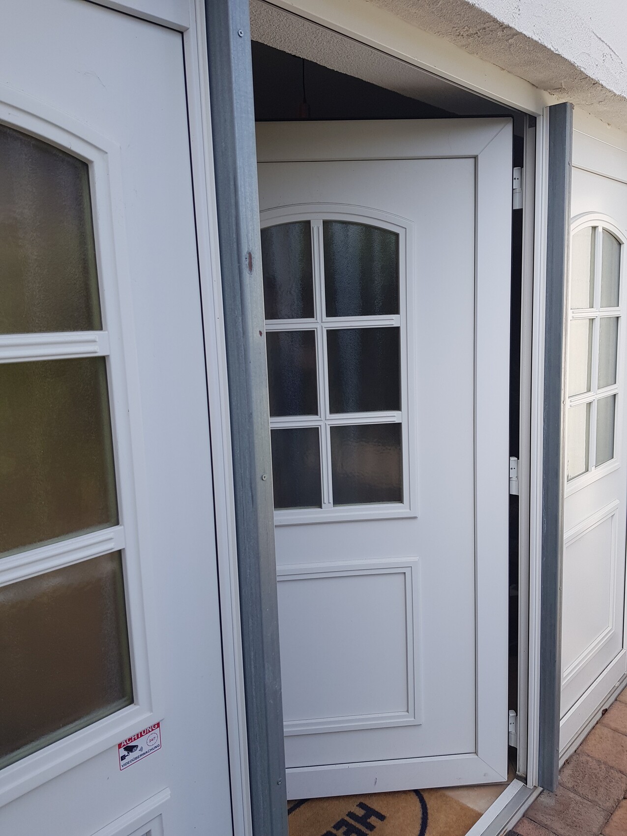 Weiße Haustür mit sechs Fenstern im Gitter-Design, offen im Eingangsbereich.