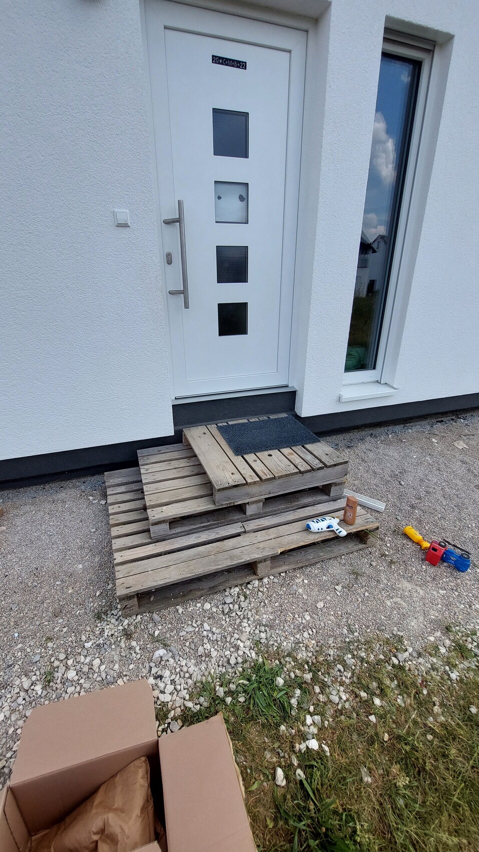 Weiße Haustür mit vier quadratischen Fenstern; Paletten-Treppe vor dem Eingang, Spielzeug daneben.