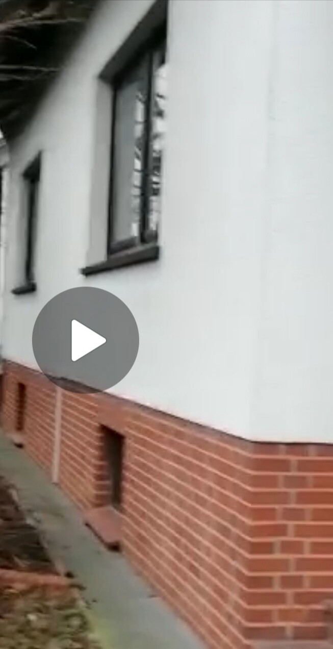 Außenansicht eines Hauses mit weißer Fassade über rotem Klinker, Fenster mit schwarzen Rahmen.