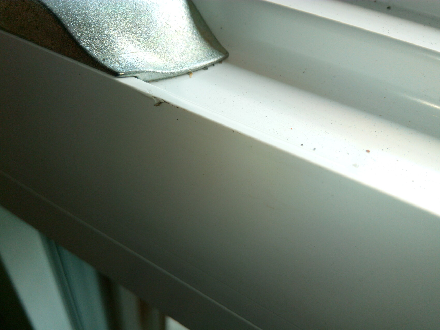 Nahaufnahme eines weißen Fensterrahmens mit Metallclip und Staubkörnern.