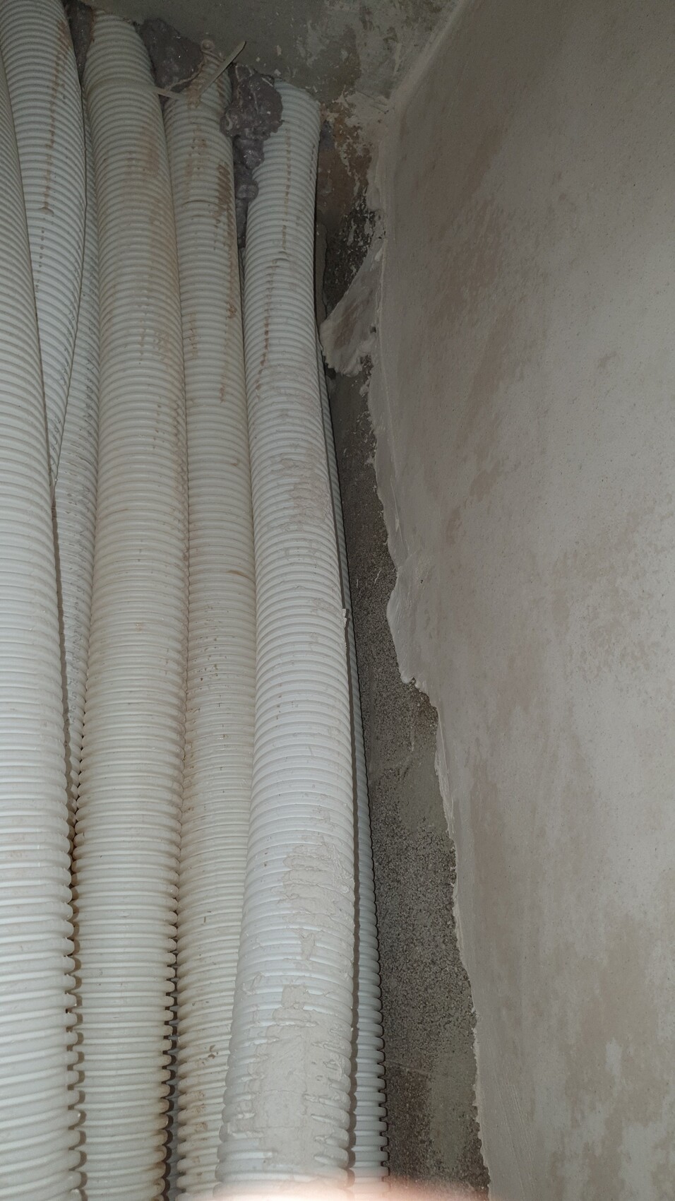 Mehrere weiße, gerippte Rohre stehen dicht an einer rauen Wand in einem Baubereich.