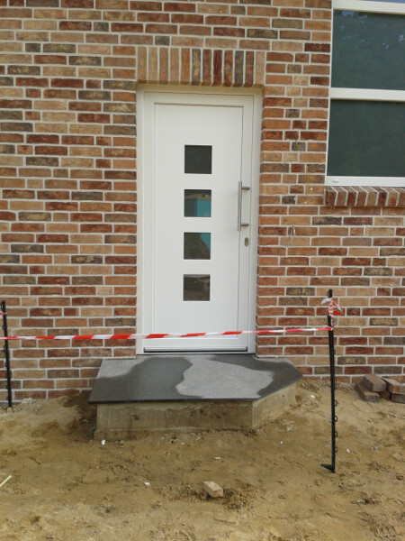 Weiße Tür mit vier quadratischen Fenstern in Backsteinfassade, Absperrband davor.