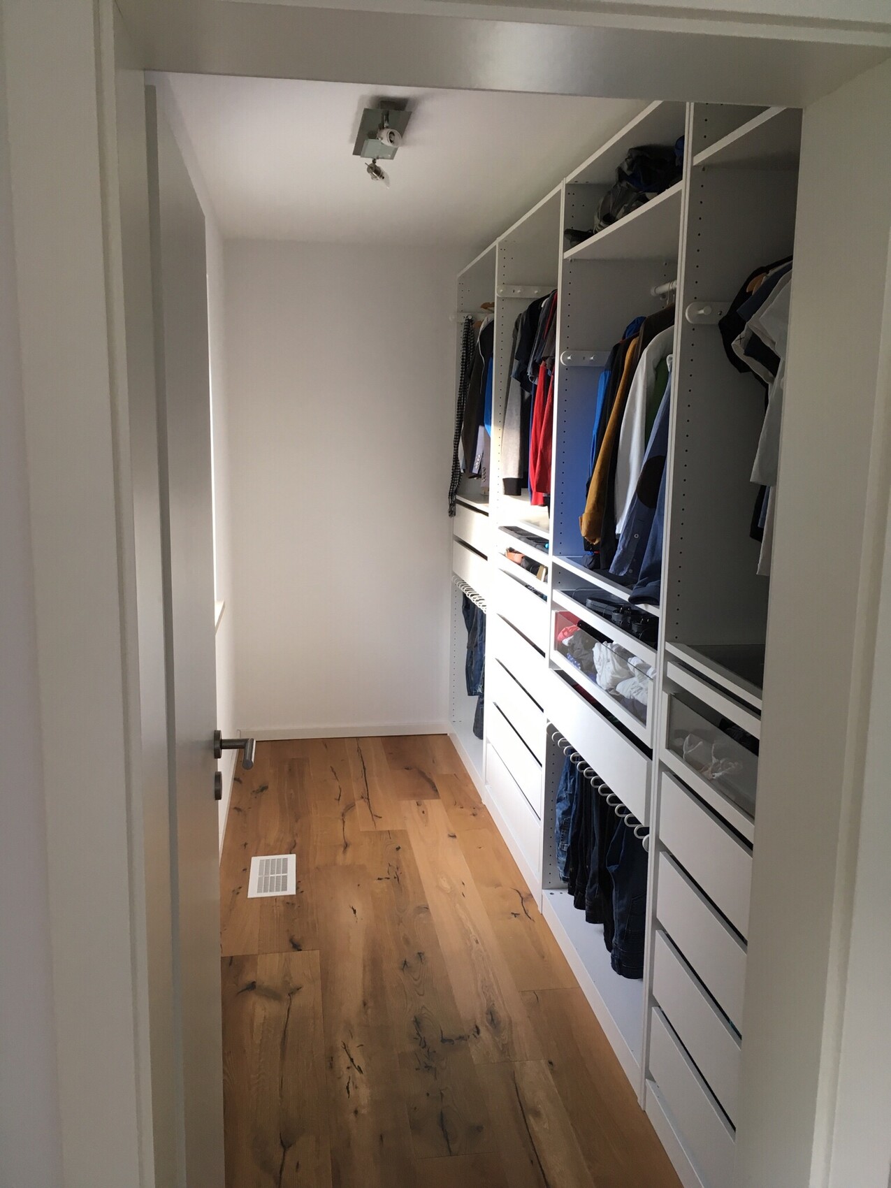 Weiße begehbare Garderobe mit Regalen, Kleiderstangen und Holzboden