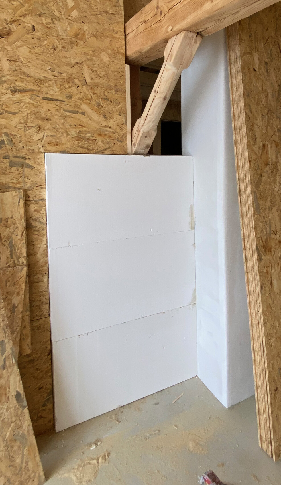 Baustellen-Ecke: Weiße Dämmplatten lehnen an OSB-Wand, Holzbalken oben.