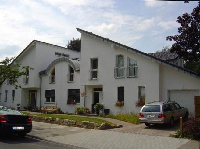 Weisse Wohnhausfassade mit grossen Fenstern, Einfahrt und parkenden Autos