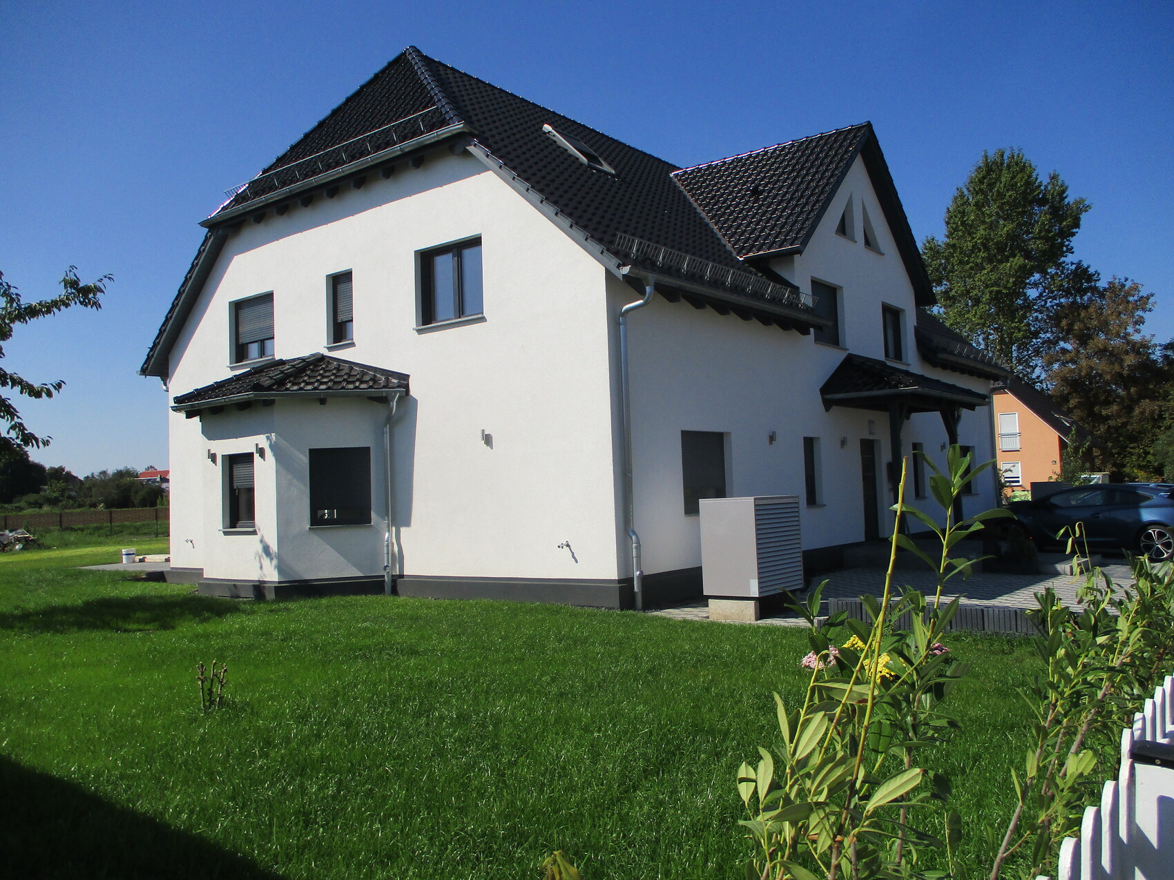 Weißes, zweistöckiges Haus mit schwarzem Ziegeldach, grünem Rasen und Auto auf der Einfahrt