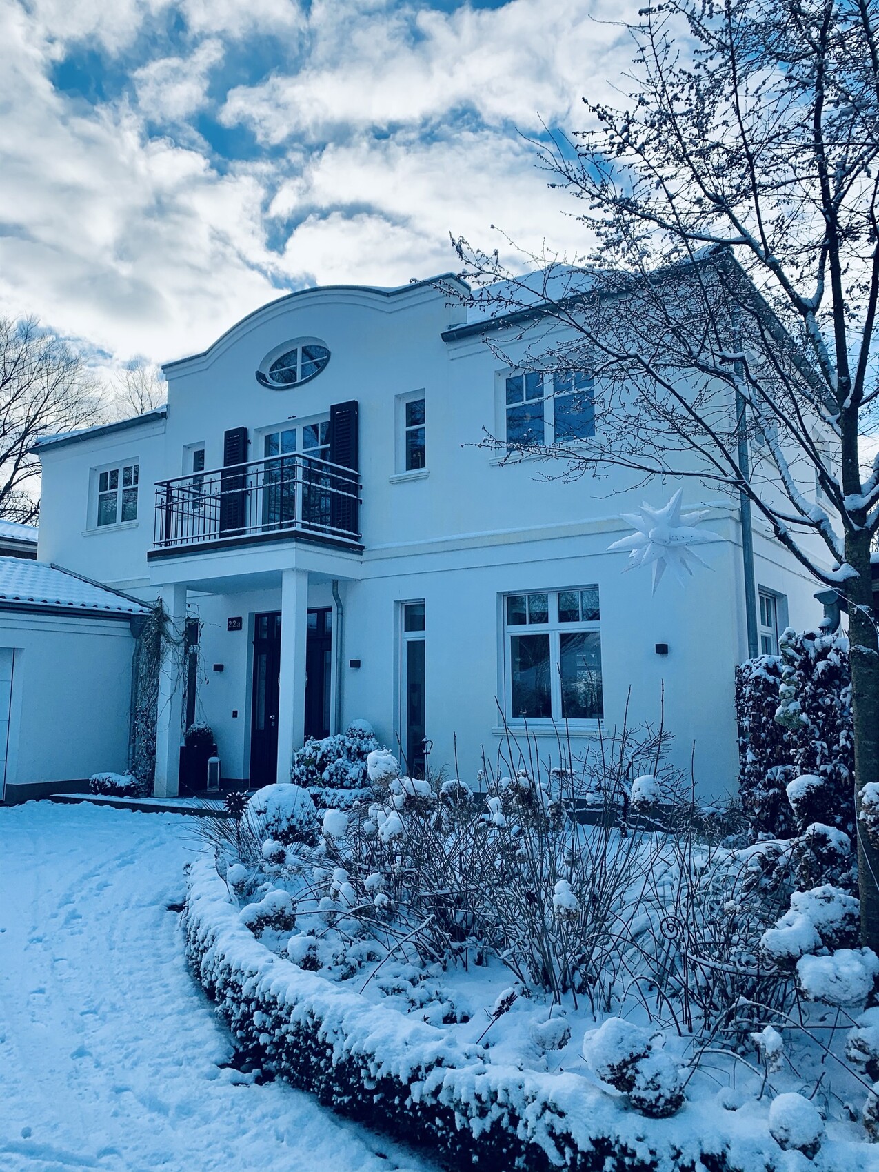 Weiße, zweistöckige Villa im Winter mit verschneitem Garten, Balkon und Stern-Dekor.