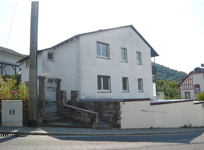 Weißes zweistöckiges Haus mit Steinfundament, Gartentor und Treppenaufgang zur Straße.