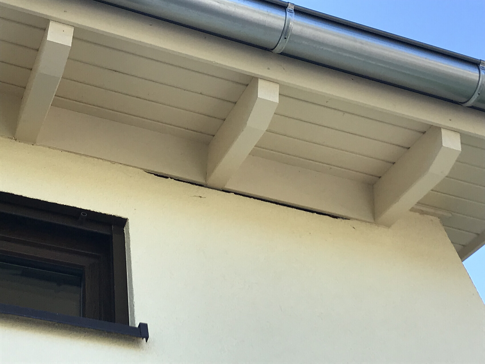 Weiße Holzbalken unter dem Dachüberstand, Dachrinne; Fenster mit dunklem Rahmen