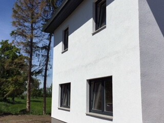 Weiße Hausfassade mit Fenstern neben Bäumen bei sonnigem Tag.