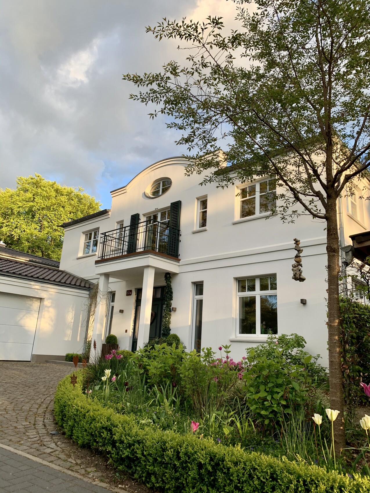 Weiße Villa mit Balkon, grünen Fensterläden und Tulpen im Garten