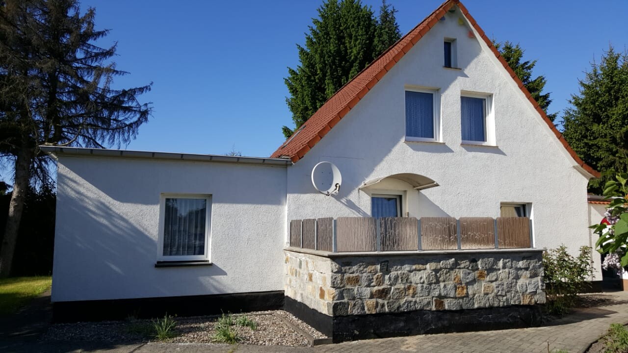 Weißes Einfamilienhaus mit rotem Satteldach, Steinmauer und Satellitenschüssel im Garten