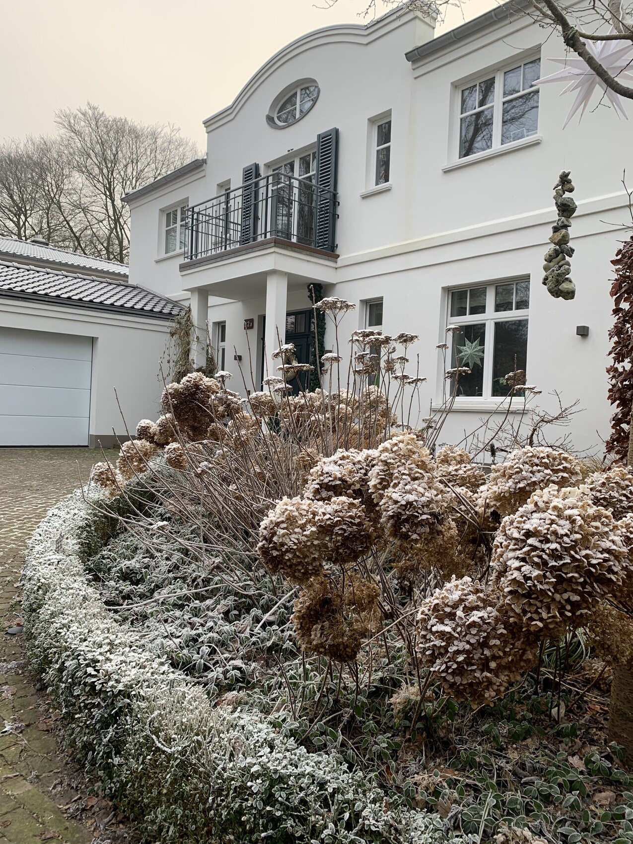 Weiße Villa mit Balkon, frostige Hortensien im Garten, winterliche Stimmung.
