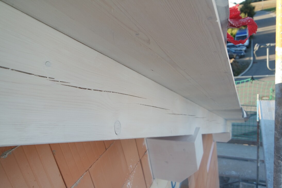 Weiß gestrichene Holzbalken an einer Baustellenfassade, Blick von unten auf das Bauwerk.