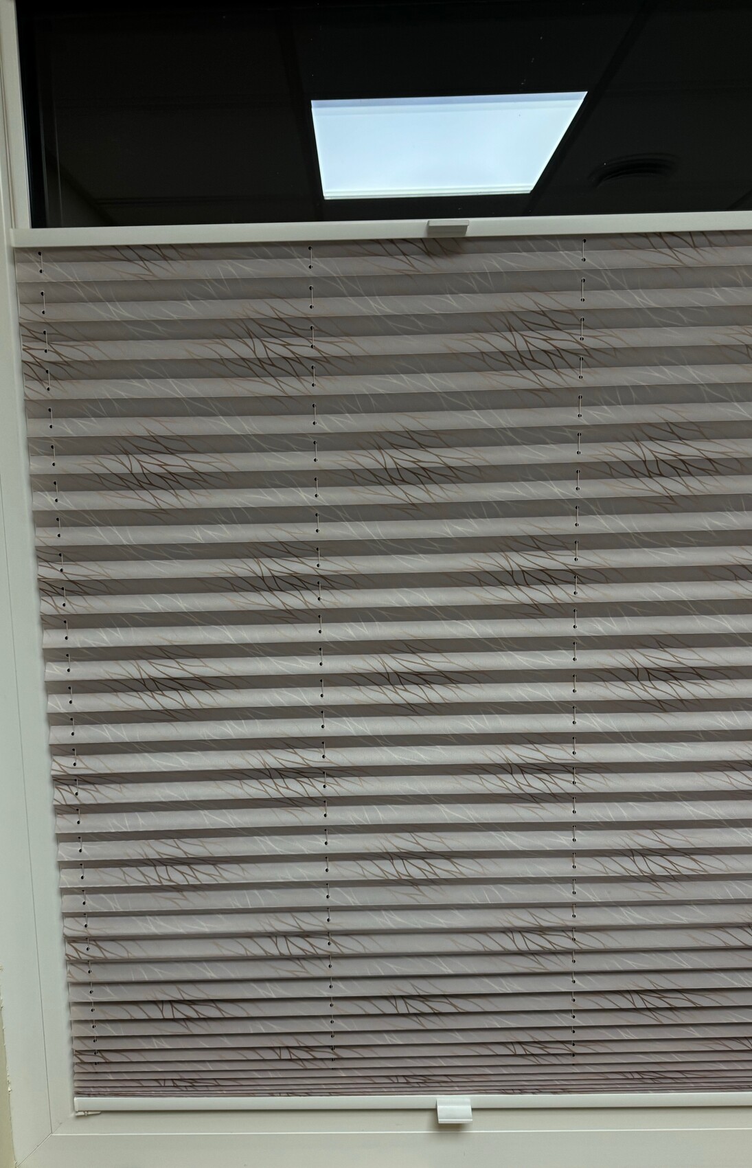 Horizontale Jalousien vor einem Fenster; oben ein Dachfenster lässt Licht herein.
