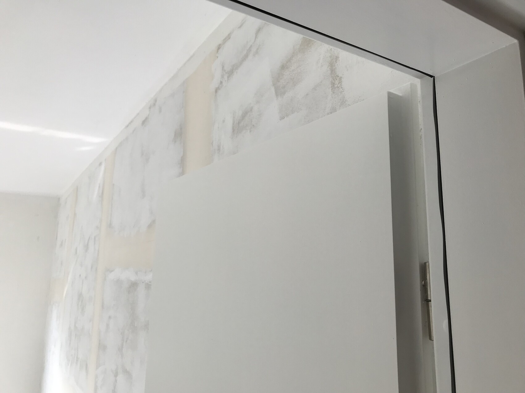 Weiße Innentür im Vordergrund, leicht geöffnet; dahinter hellgraue, gemusterte Wand.
