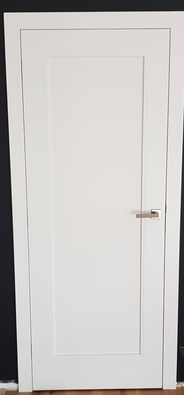Weiße Innentür mit modernem Metallgriff vor dunkler Wand