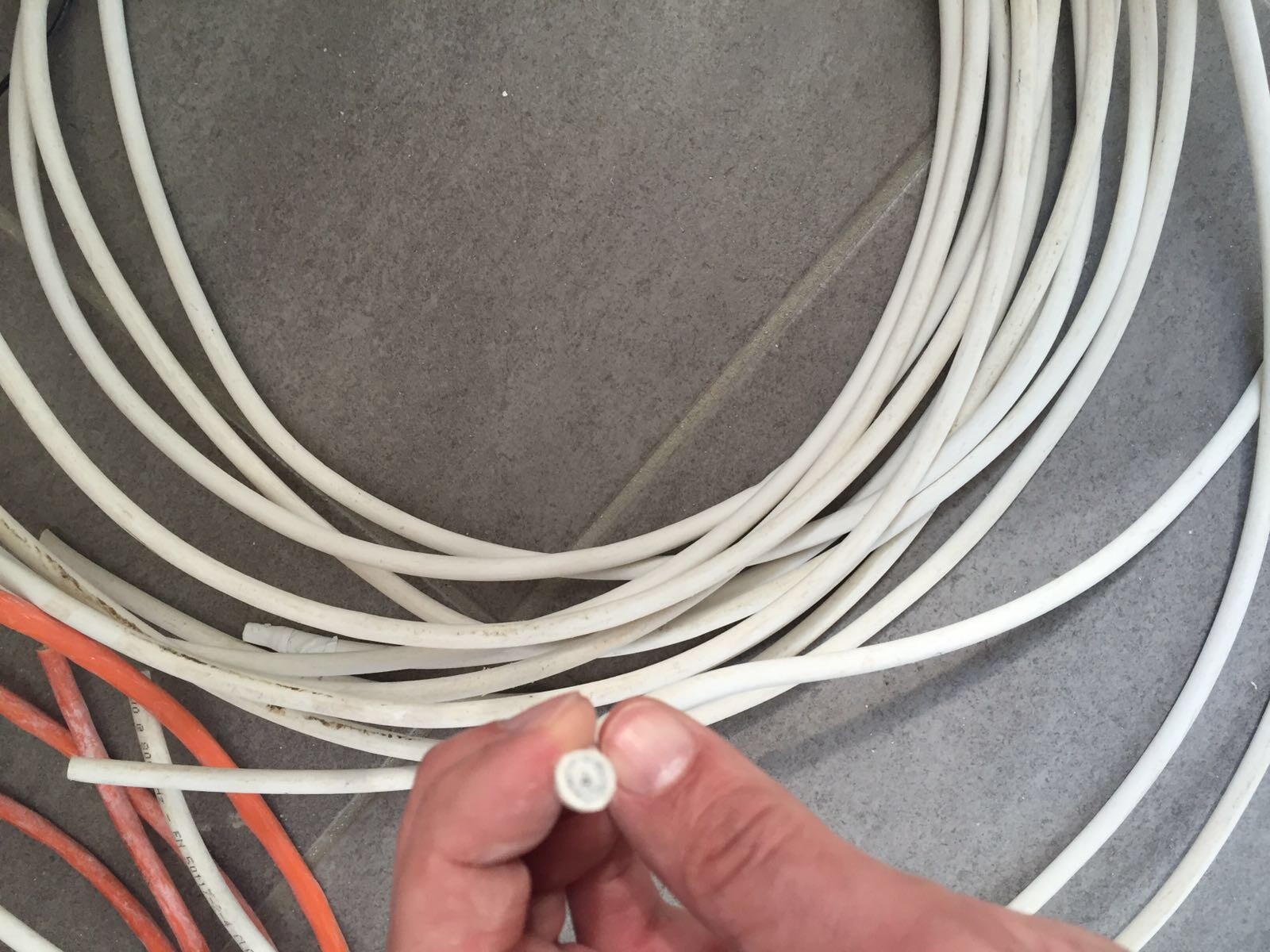 Nahaufnahme: Hand hält weißes Kabelende; viele weiße Kabel, orange Kabel liegen auf dem Boden.
