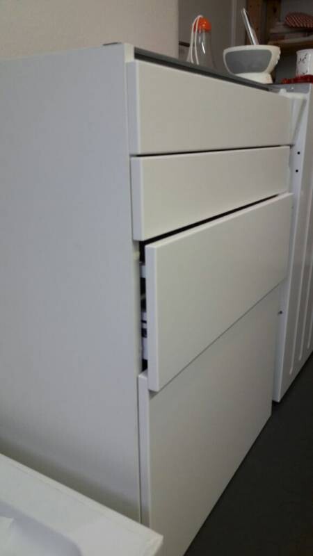 Weiße Kommode mit drei Schubladen; eine Schublade ist leicht geöffnet, steht in einem Raum.