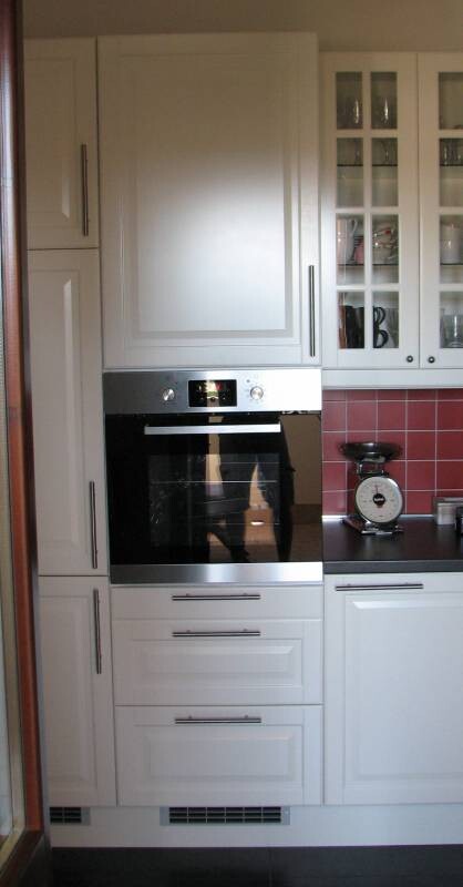 Weiße Küchenzeile mit Einbau-Backofen, Glasvitrinen und roter Fliesenrückwand