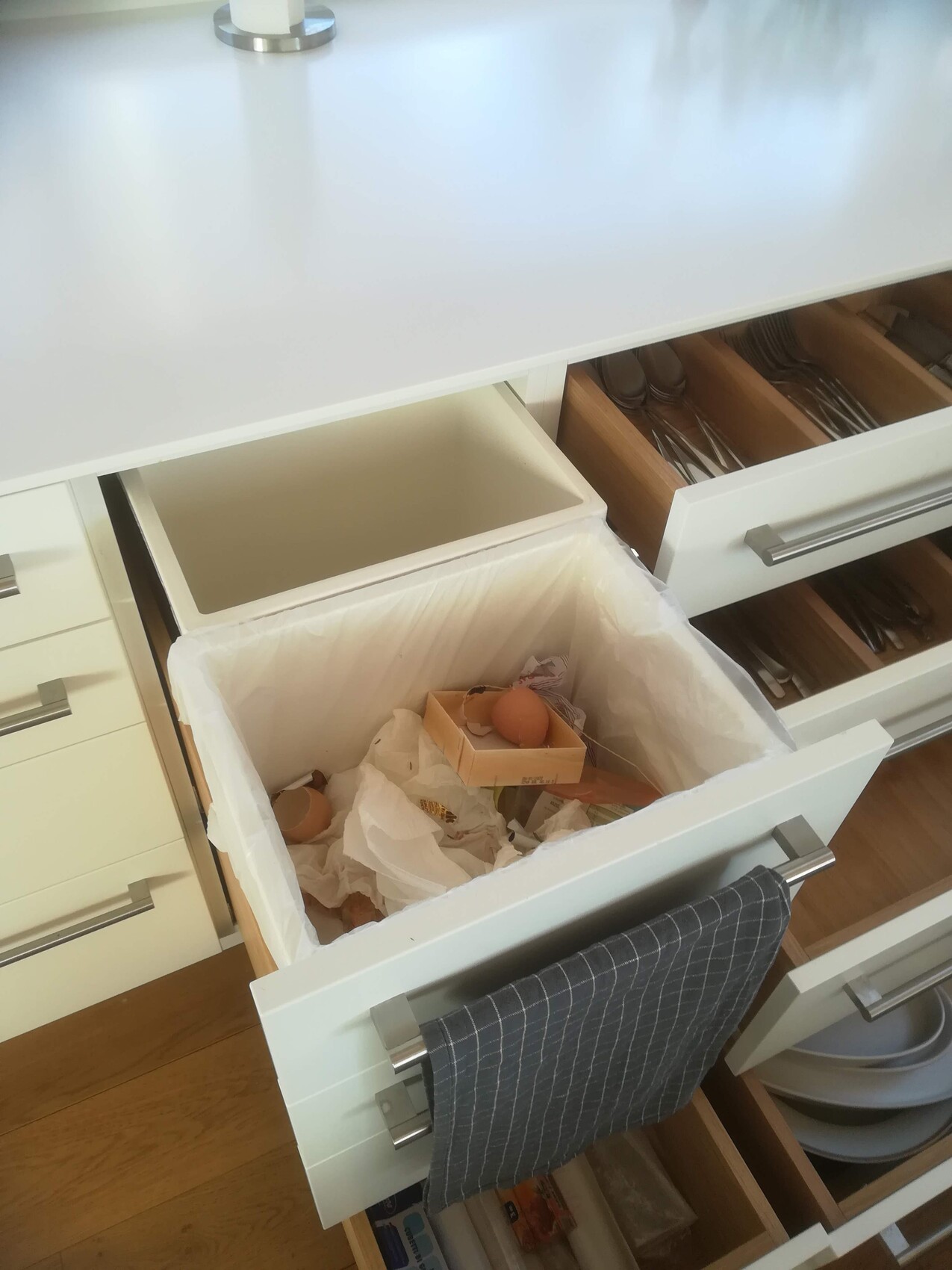 Offene Küchenschublade mit Müllbehälter, Eierkarton und Papier im Müll.