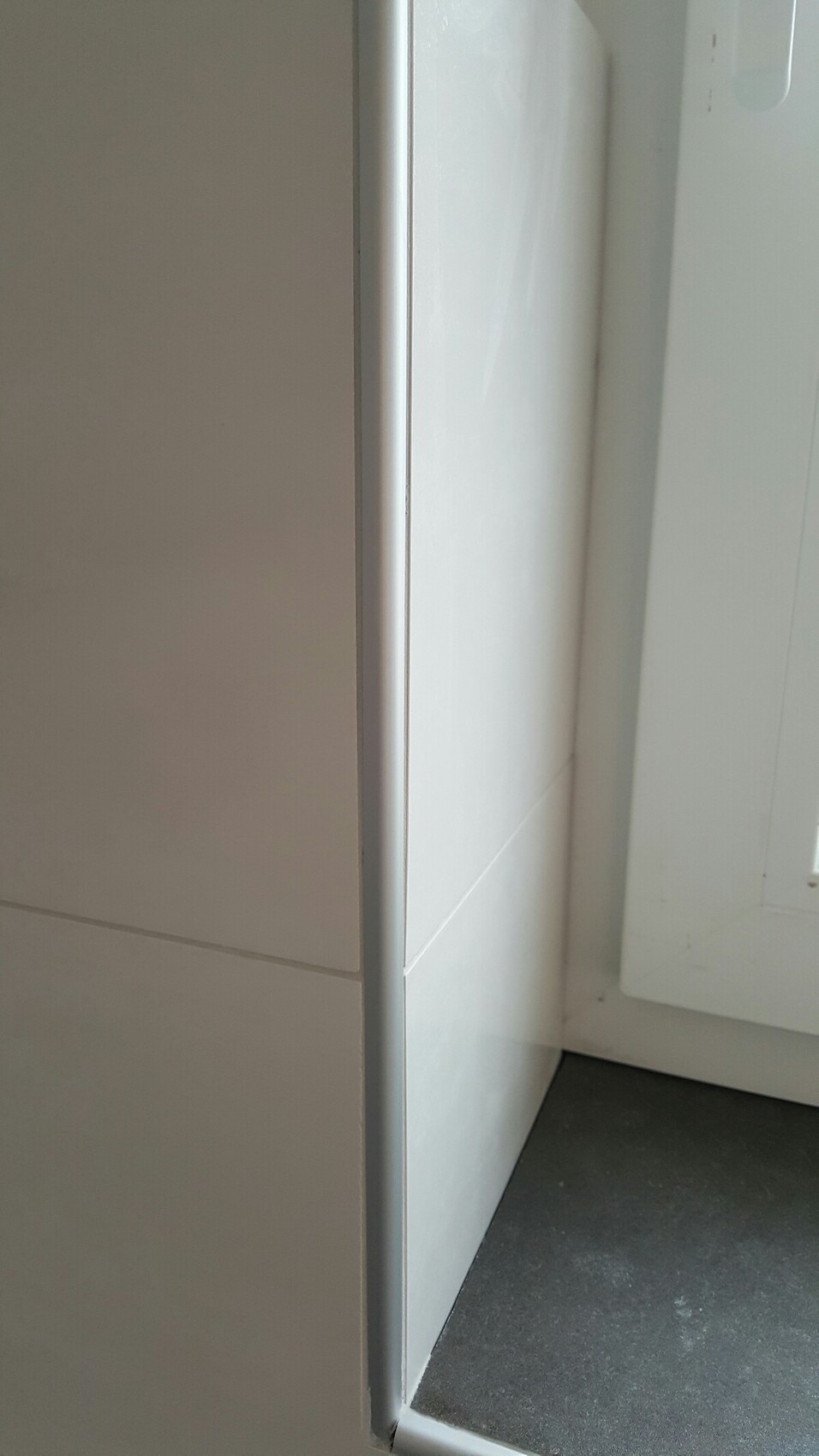 Weiße Küchenfronten mit Türpaneel, Fensterrahmen und dunklem Boden.