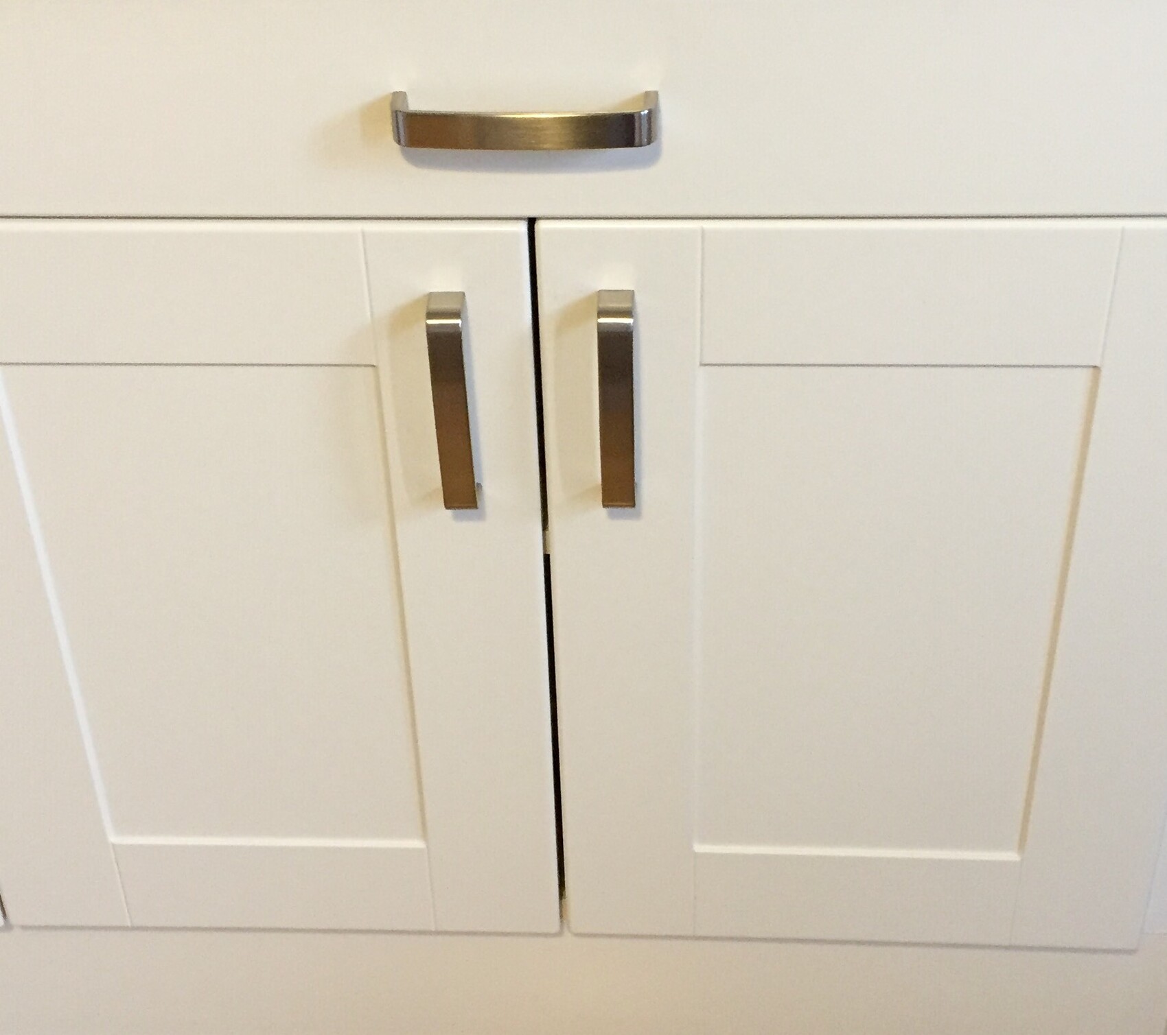 Weiße Küchenschränke mit silbernen Edelstahlgriffen.