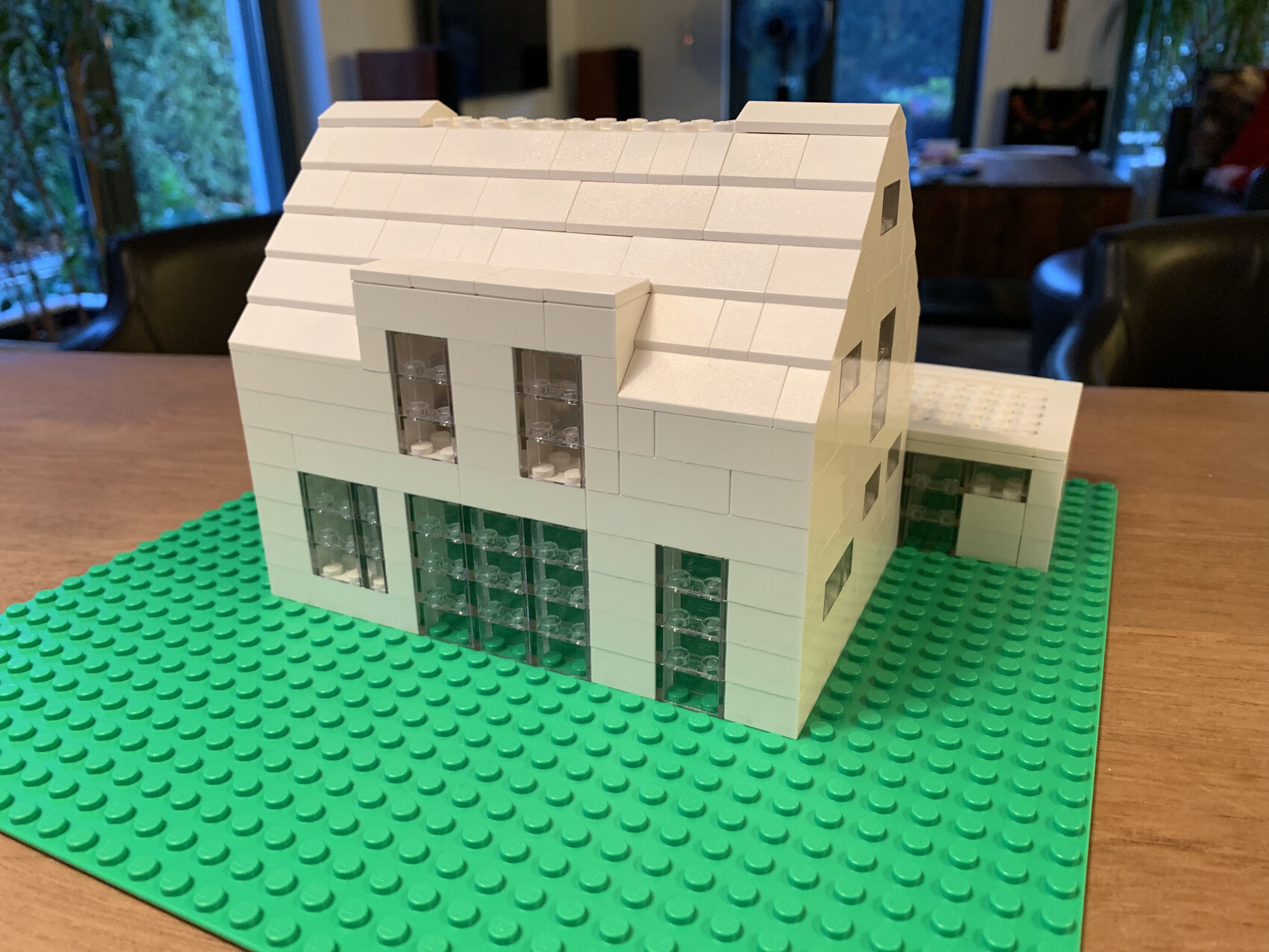 Weißes LEGO-Haus mit schrägem Dach auf grüner Grundplatte, Fenster aus transparenten Steinen.