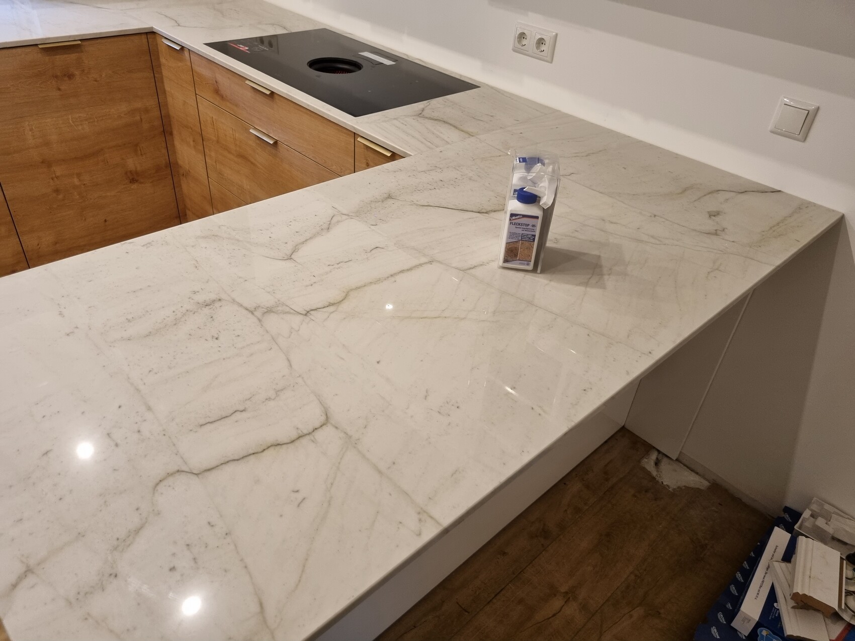 Eine Kücheninsel mit weißer Marmor-Arbeitsplatte, Holzschränken, Reinigungsflasche in der Mitte.