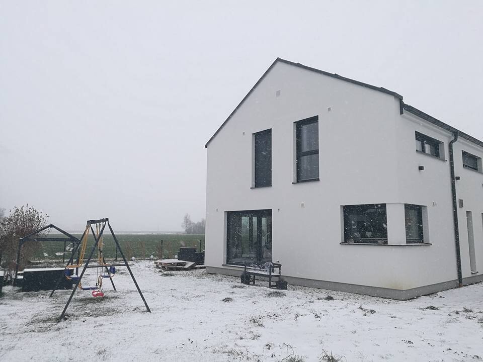 Weiße moderne Hausfront im Schnee mit großen Fenstern und Spielgeräten im Vorgarten
