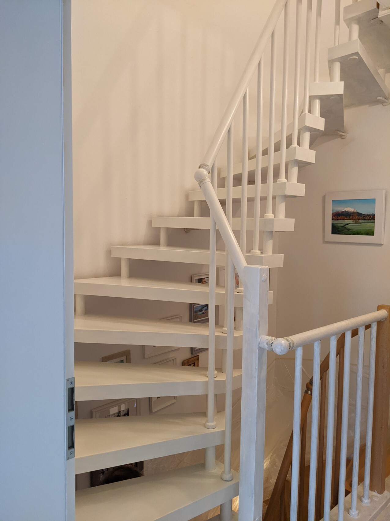 Weiße Innen-Treppe mit offenen Stufen und Geländer, Wandbilder im Hintergrund.