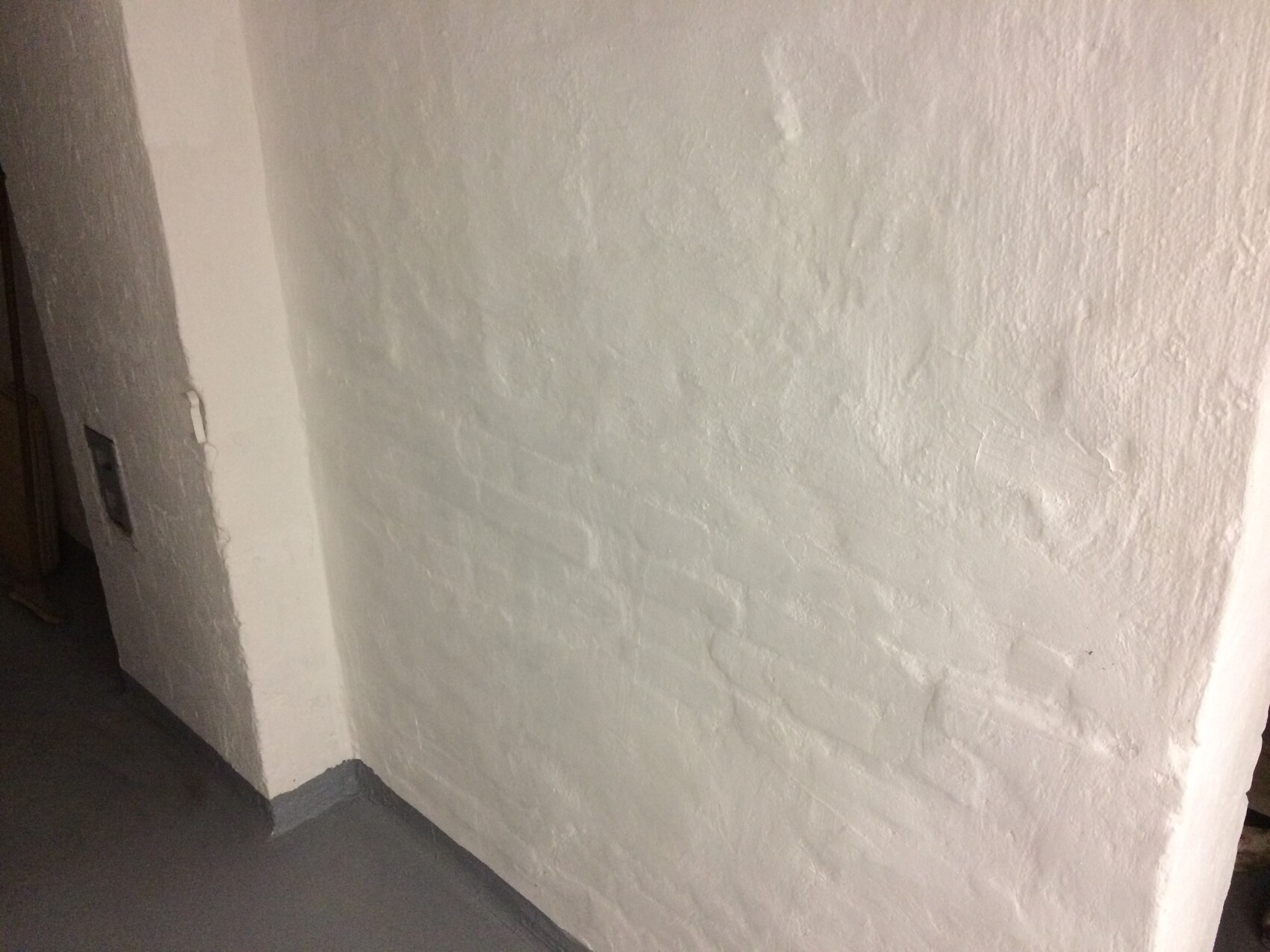 Weiße Putzwand in einer Innenraum-Ecke mit rauer Oberflaeche