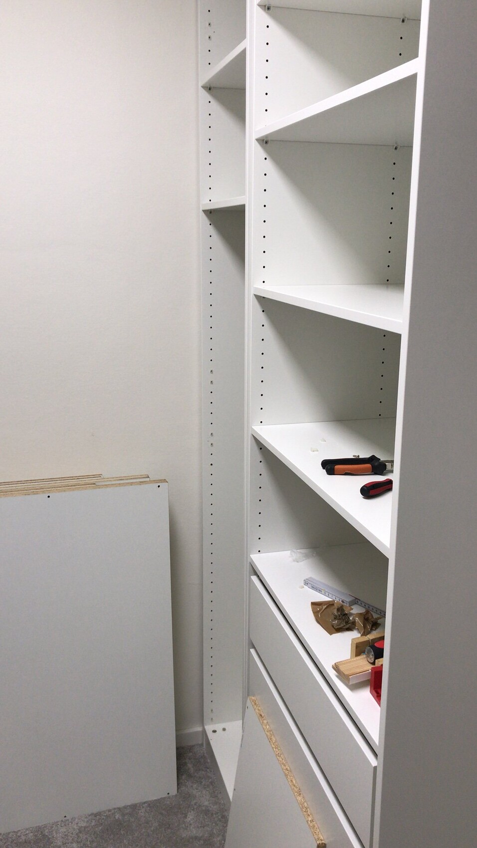 Weiße, hohe Regalwand mit verstellbaren Böden; Schraubwerkzeuge auf der unteren Ablage.