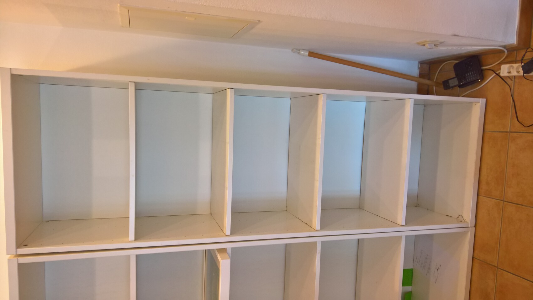 Weisses offenes Regal mit mehreren Brettern in einem hellen Wohnraum, neben Steckdosenleiste.