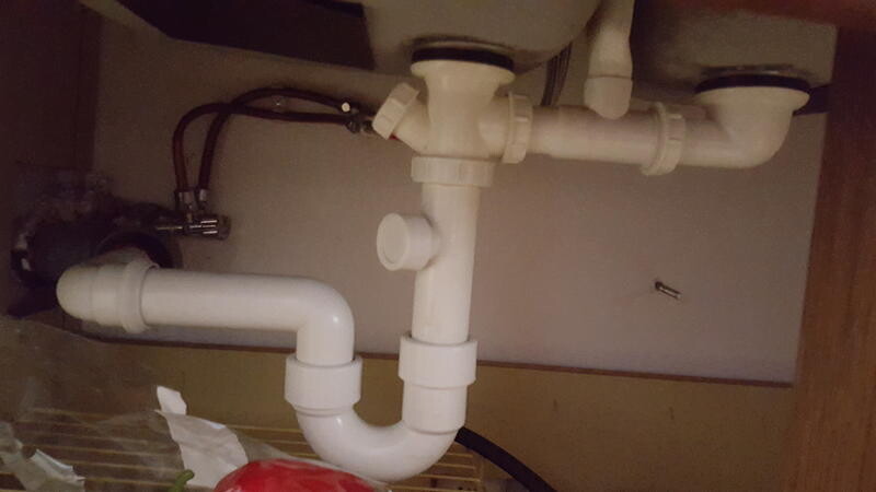 Unter dem Spülbecken sichtbare weiße PVC-Rohrleitungen und Siphon