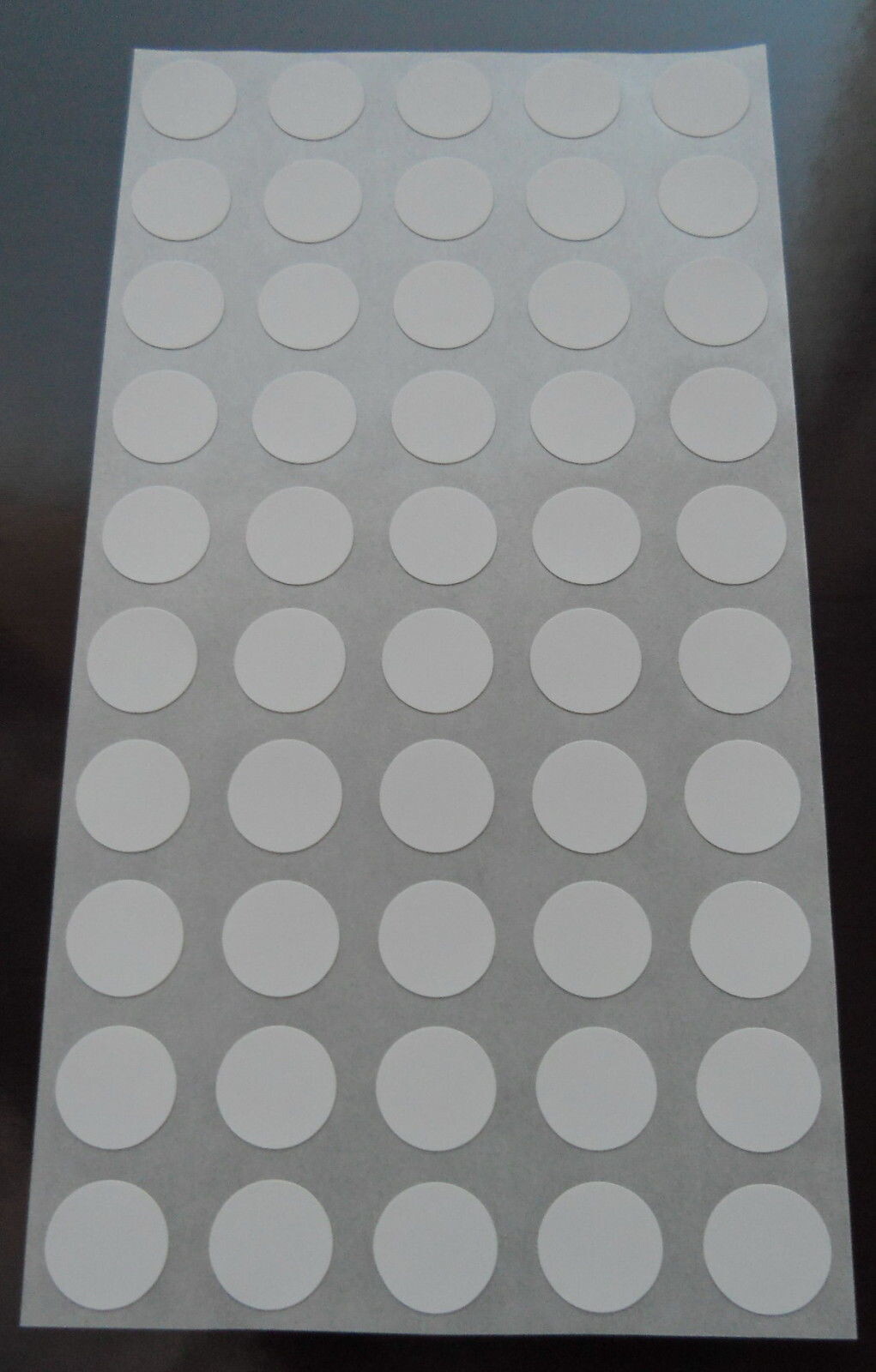 Ein Blatt mit vielen weißen, runden Klebeetiketten auf grauem Trägerpapier.