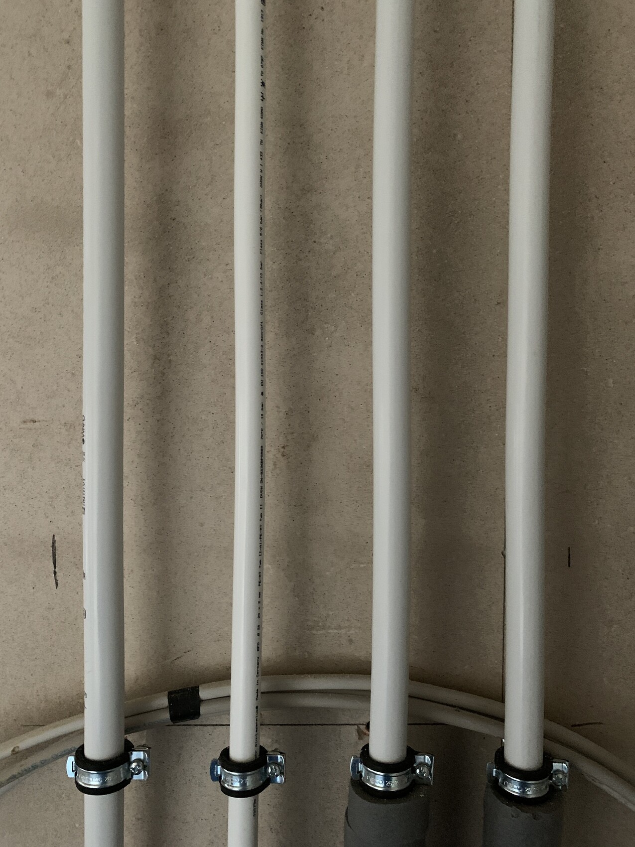 Mehrere vertikale weiße PVC-Rohre, an der Wand befestigt, mit Metallklemmen unten.