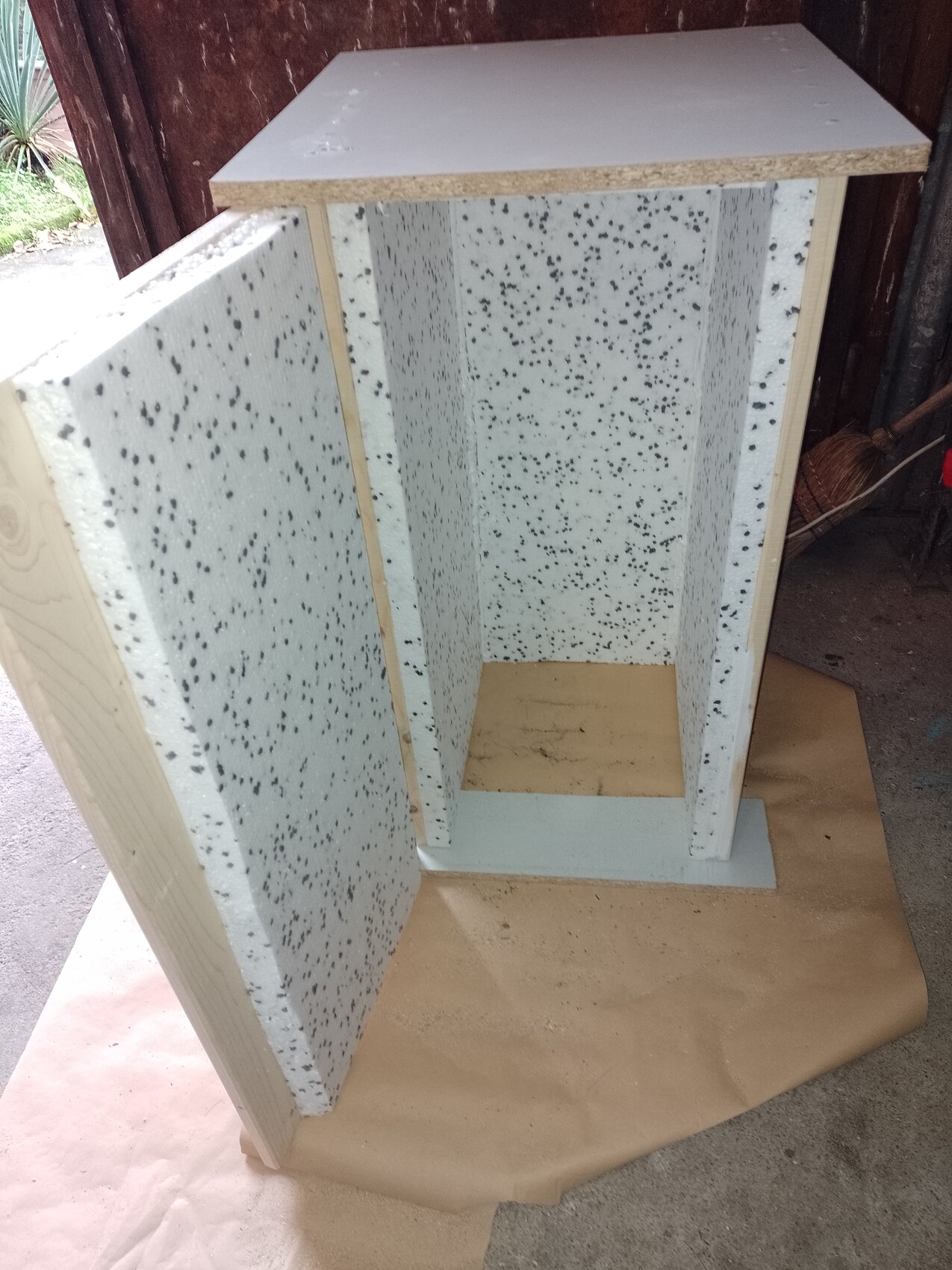 Offener Möbelrahmen aus weißen, gesprenkelten Schaumstoffplatten mit Holztop, Innenraum leer.