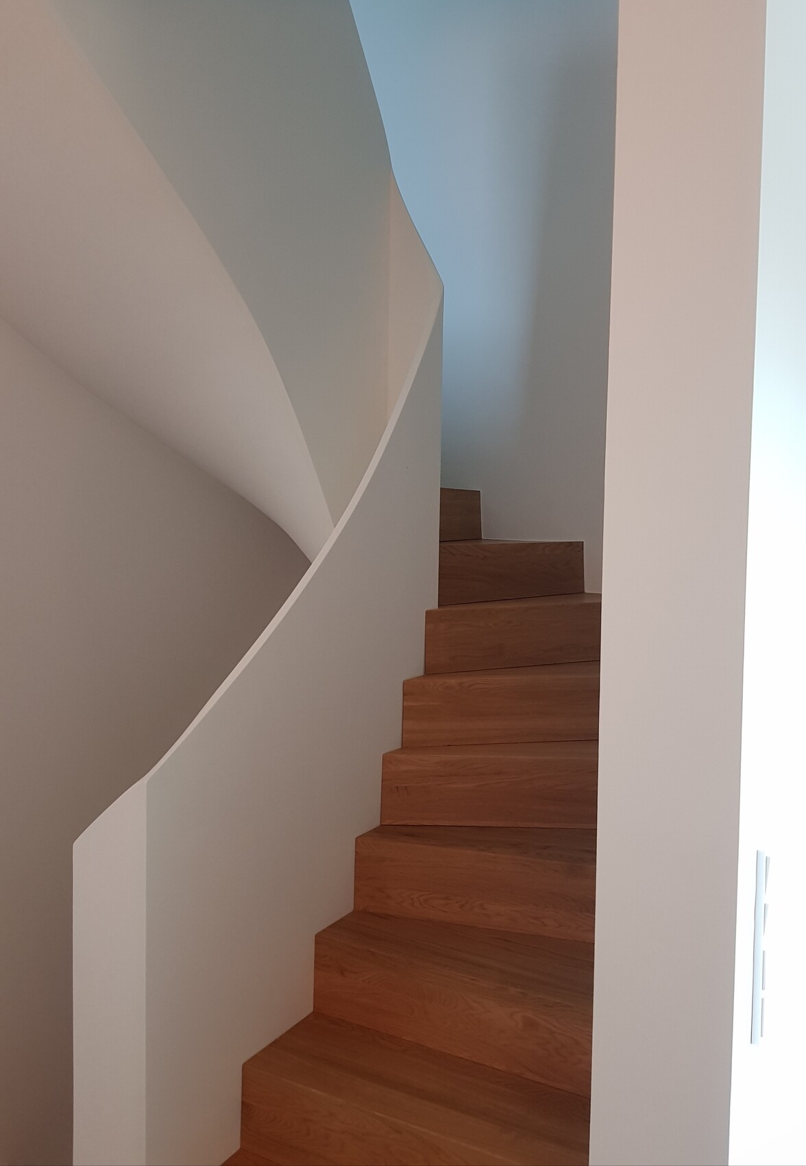 Moderne Holztreppe mit sichtbaren Holzstufen vor weißer gebogener Wand im Innenraum