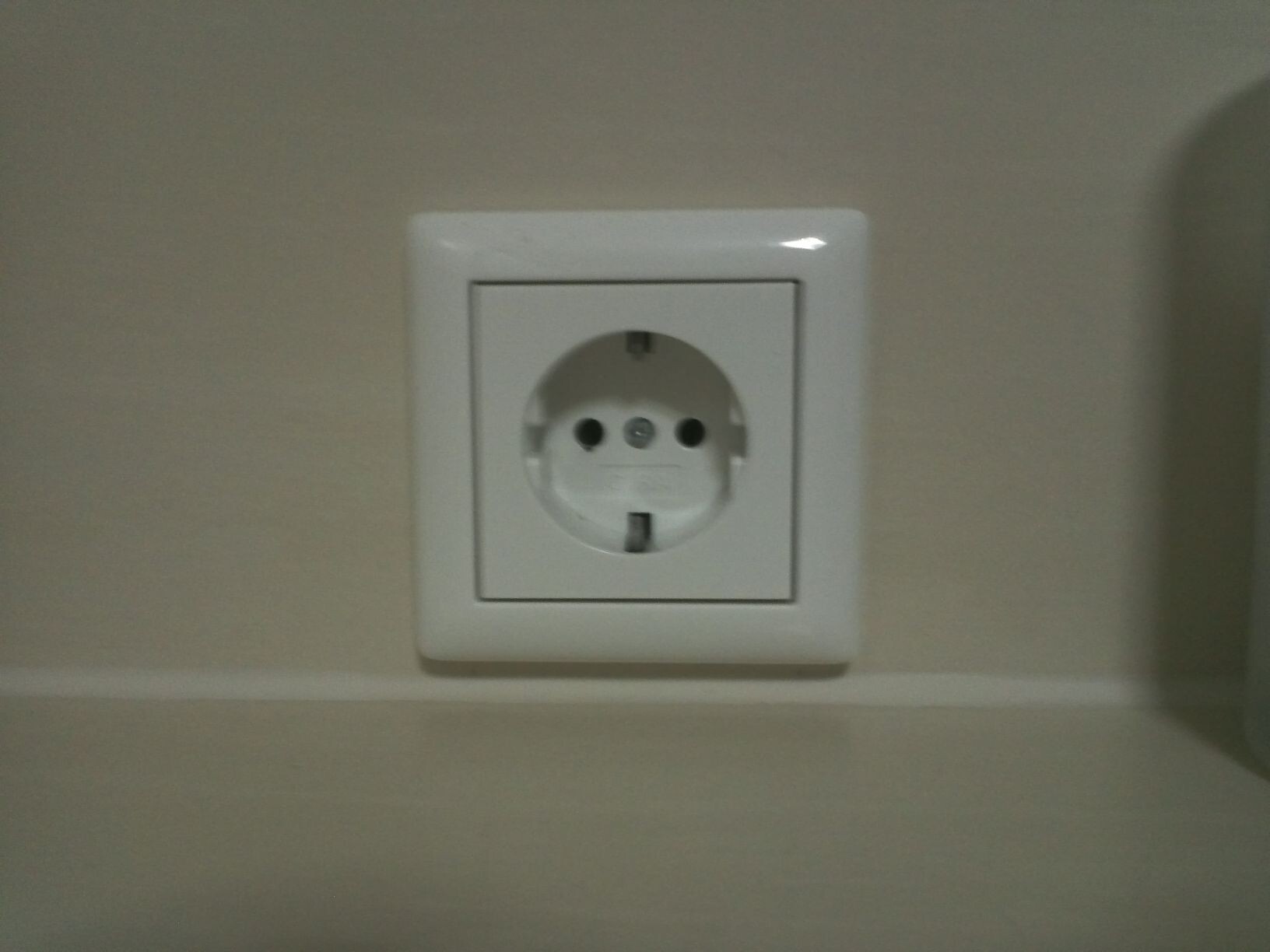 Weiße europäische Steckdose (Schuko) in quadratischem Rahmen an der Wand.