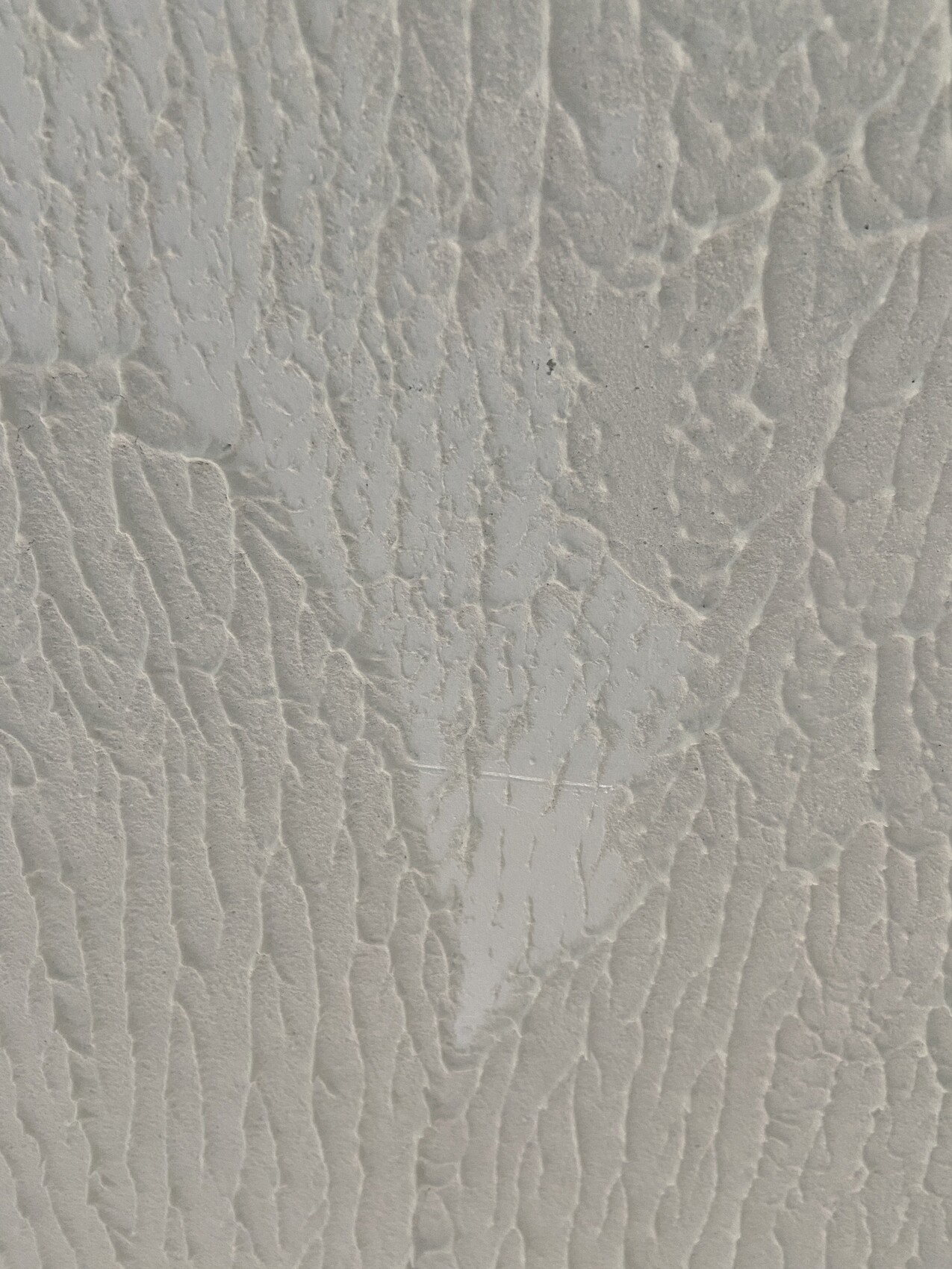 Weiße Putzwand mit feinen, unregelmäßigen Rissen und texturierter Oberfläche.