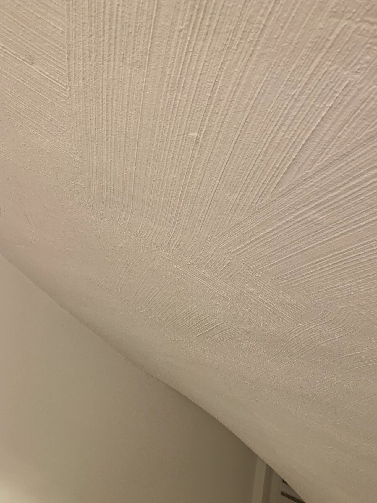 Weiße Stuckdecke mit strahlenförmigen Mustern in der Ecke von Decke und Wand.