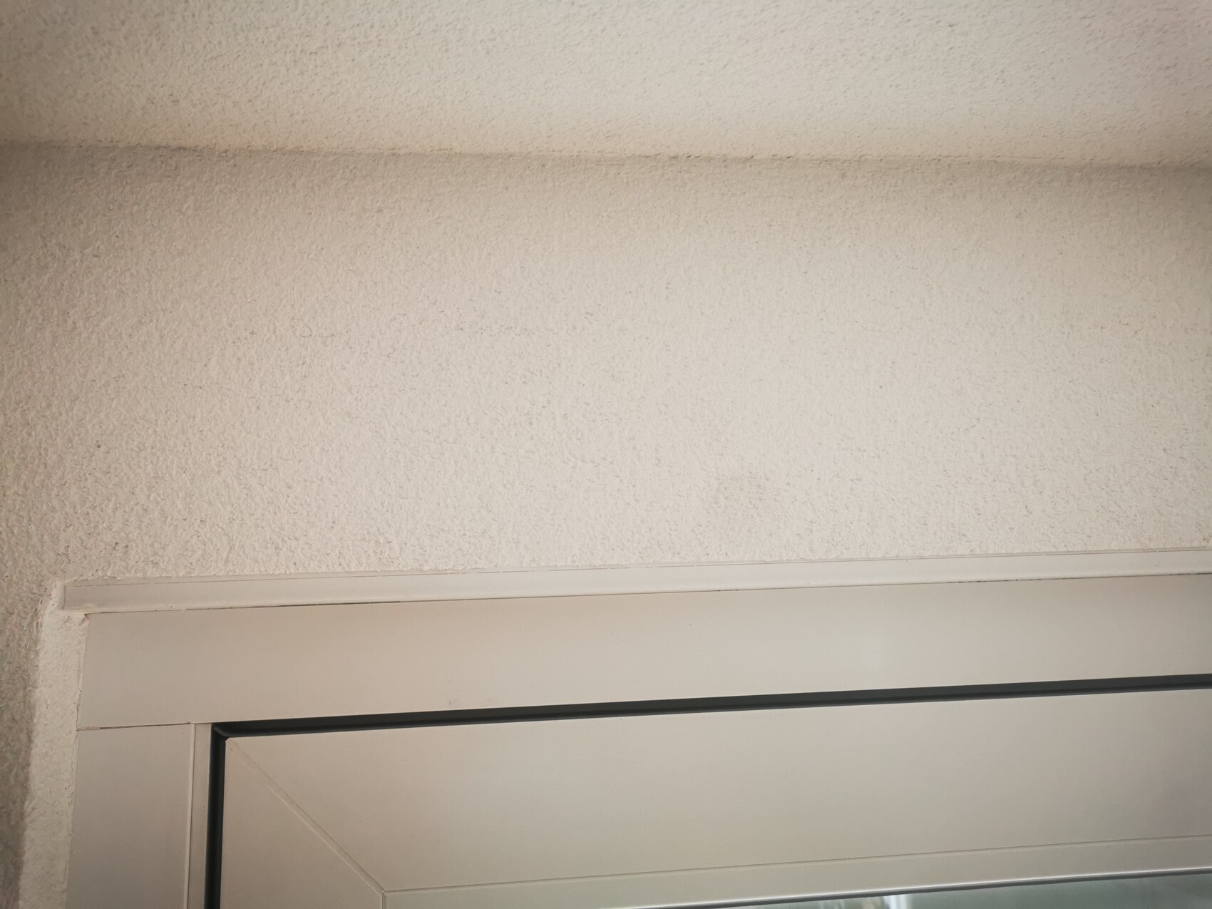 Weißer Türrahmen im unteren Bildbereich vor grob strukturierter weißer Wand.