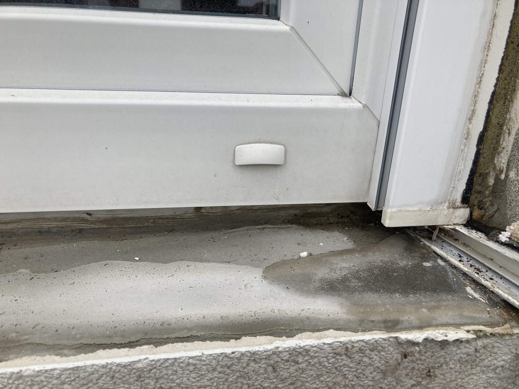 Weiße Tür mit kleinem Griff; Türschwelle und feuchter, schmutziger Außenboden.